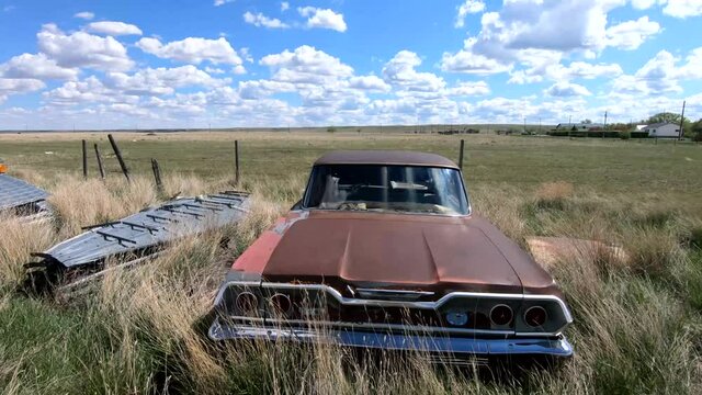 Old rusty car sitting in a grassy field on a sunny day during the summer with a blue sky and clouds overhead.