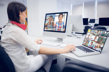 Caucasian female teacher using computer and laptop on video call with school children