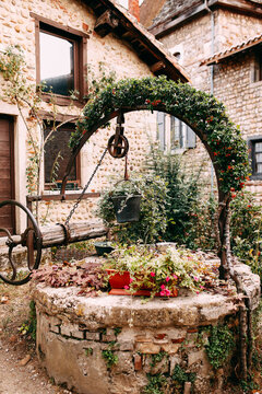 Old wooden stone well with red flower arch and ivy in Perouges, France