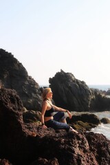 The girl sits on a rock near the surf and looks into the distance