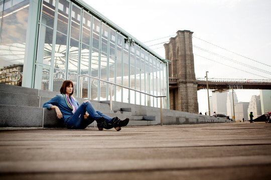 Thoughtful woman sitting by Jane's Carousel against Brooklyn Bridge