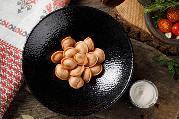 Traditional Russian dumplings, tomato paste for red dough. Still life on a wooden board. Close-up.