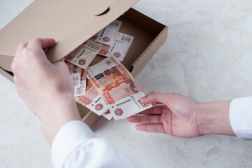A woman's hand pulls out from a cardboard box five thousand rubles, the concept of profit from the sale of pizza
