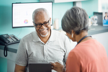 Happy senior male patient talking to female doctor in clinic