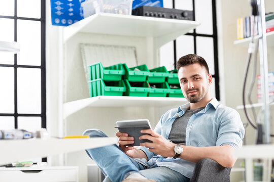 Portrait of confident engineer using tablet computer while sitting in electronics industry