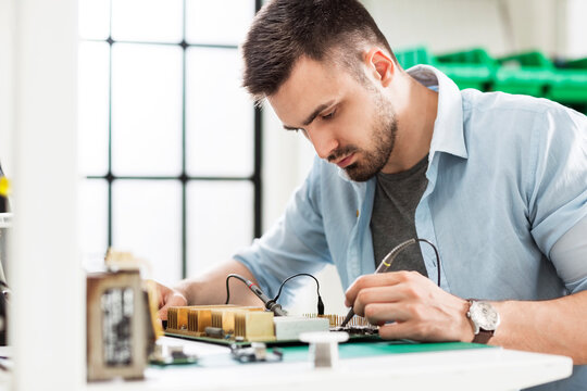 Serious technician soldering circuit board at table in electronics industry