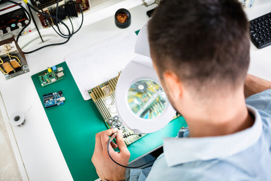 Technician soldering circuit board using magnifying glass at table