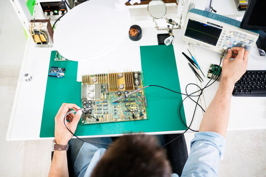 High angle view of technician checking circuit board at table in electronics industry