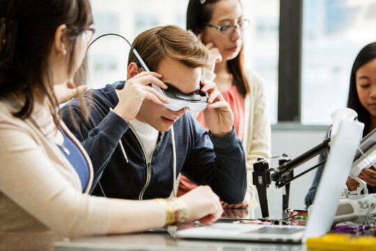 Male student wearing virtual reality glasses while sitting by friends in classroom