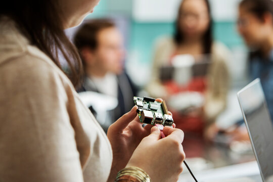 Cropped image of student attaching cable to circuit board with friends and teacher in background