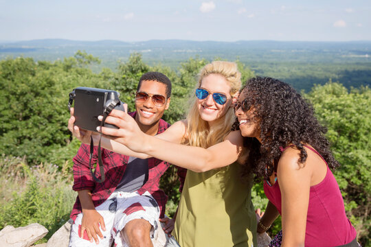 Happy friends taking selfie through instant camera on mountain
