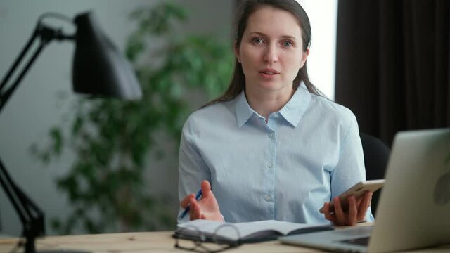 An adult young Caucasian female teacher tells a topic on camera, a blogger works from home, looks into the camera and conducts a video conference or online lesson, blog entry lifestyle vlog.