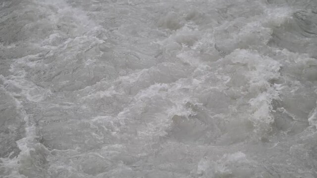Fast streaming gray melted water in a small river and sloshing on the rocks and stones in Lauterbrunnen Switserland. Close-up shot