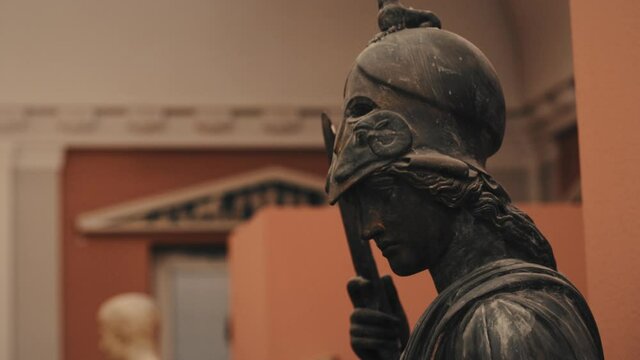 Close up of an ancient antique black male statue wearing a helmet and holding a knife in a museum with moody warm lights. Smooth panning shot, racking focus. Shot in 4K.