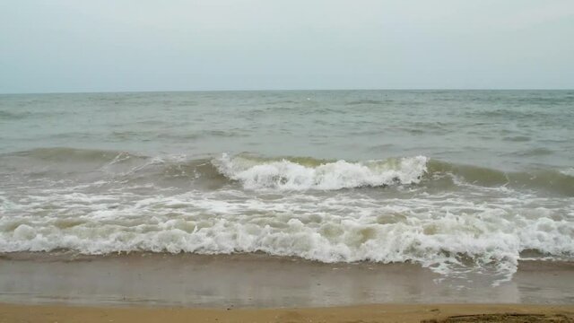 Small waves comes in on a sandy beach and the weather is not so fine.