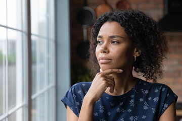 Fototapeta na wymiar Close up thoughtful African American woman looking out window to aside, touching chin, dreamy young female lost in thoughts, planning, visualizing future, businesswoman thinking, making decision
