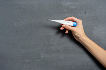 a woman's hand holds an electronic thermometer on a gray textured background. concept of medical instruments. Copy space