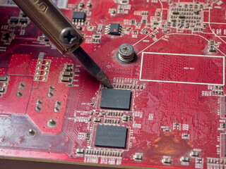 A repairman solders a printed circuit board of an electronic device in red color close-up. Repair...
