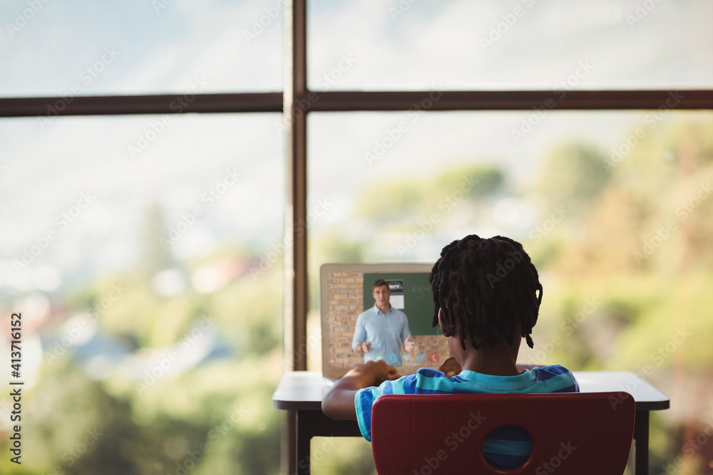 Poster Rear view of male student having a video call with male teacher on laptop at school