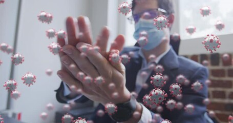 Animation of covid 19 cells floating over man wearing face mask, sanitizing his hands in office - Powered by Adobe