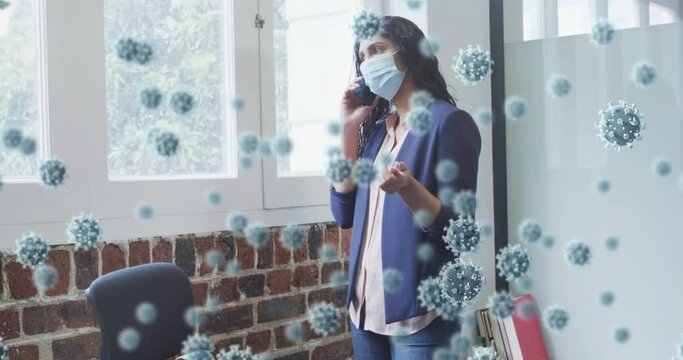Animation of covid 19 cells floating over man wearing face mask, using smartphone in office