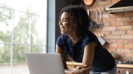 Close up overjoyed dreamy African American woman using laptop, standing, laughing businesswoman or...