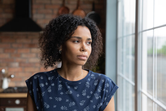 Close up upset African American woman looking to aside out window, standing at home, serious thoughtful young female lost in thoughts, thinking about problem, worried by break up with boyfriend