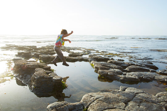 Playful boy jumping on rocks against clear sky