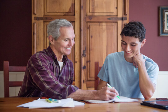Grandfather assisting grandson while studying at table in home