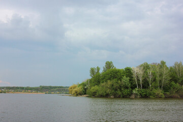 Spring landscape with river in the forest, green trees and cloudy sky.