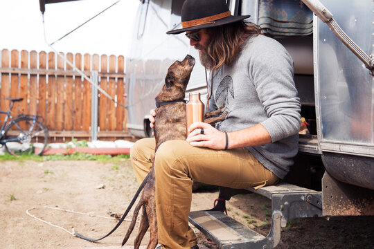 Man looking at dog while sitting on steps of camper van