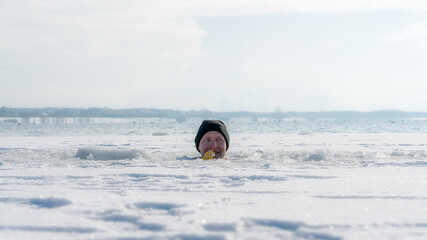 Fototapeta na wymiar Man sitting in an ice hole while eating ice cream in winter