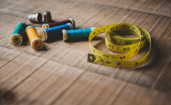 High angle view of measuring tape with colorful spools and thimbles on wooden table at workshop