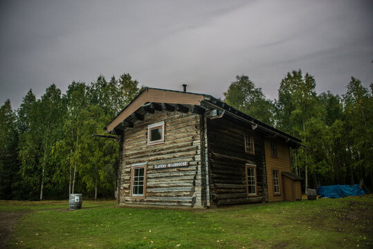 Slaven's roadhouse on field by trees at Yukon_Charley Rivers National Preserve against cloudy sky