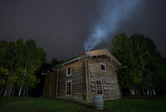 Smoke emitting from chimney on Slaven's roadhouse by trees at Yukon_Charley Rivers National Preserve against sky at night