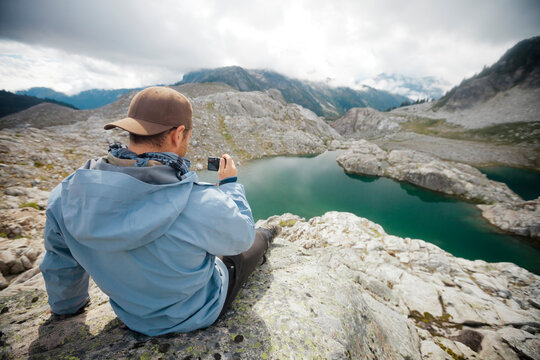 Rear view of hiker photographing while sitting on cliff at Garibaldi Provincial Park
