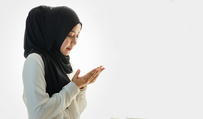 Young and beautiful Asian Muslim woman in black veil sitting on floor and praying with respect and calm manner