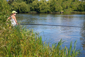 A girl with a fishing rod in her hands is fishing on the river.