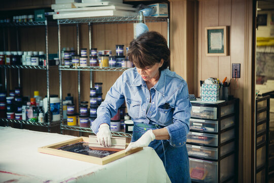 Determined craftswoman using silk screen while working at workshop
