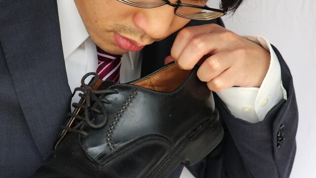 ビジネスマンが革靴のにおいを嗅ぎ、臭そうにしている
