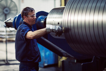 Mature worker examining in steel sheets rolling on machine at industry