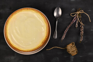 Fototapeta na wymiar Top view of whole traditional New York cheesecake with cream cheese and sour cream layer on dark background