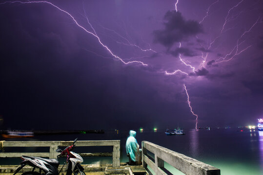 Man wearing raincoat while sitting by sea against thunderstorm lightning