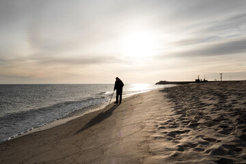 Szerokie ujęcie pod światło samotnego mężczyzny spacerującego brzegiem morza