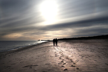 Szerokie ujęcie pod światło romantycznej pary spacerującej brzegiem morza