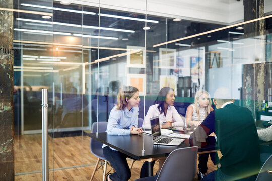 Business people at conference table during meeting seen through glass doors in office