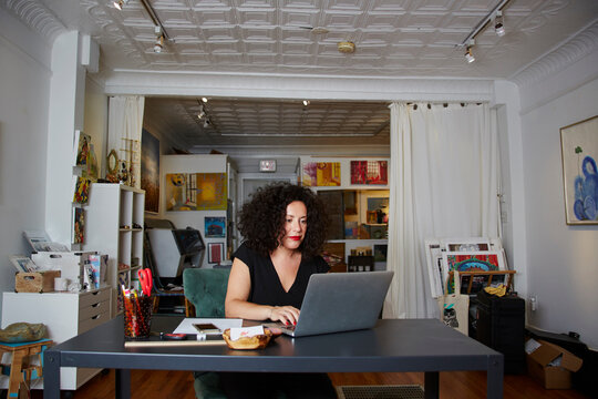 Female owner using laptop computer at table in gallery