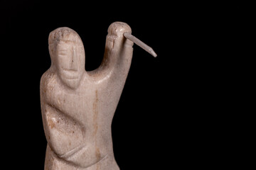 Small statue of Inuit hunter with a spear made of animal bone. Isolated on black background. Inuit...