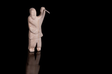 Small statue of Inuit hunter with a spear made of animal bone. Isolated on black background. Inuit art. - obrazy, fototapety, plakaty