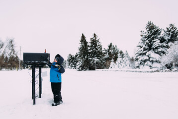 Boy in warm clothing standing on snow covered field by mailbox against clear sky
